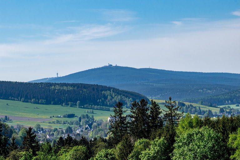 Blick ueber gruene Waelder und Wiesen zum Fichtelberg im Sommer